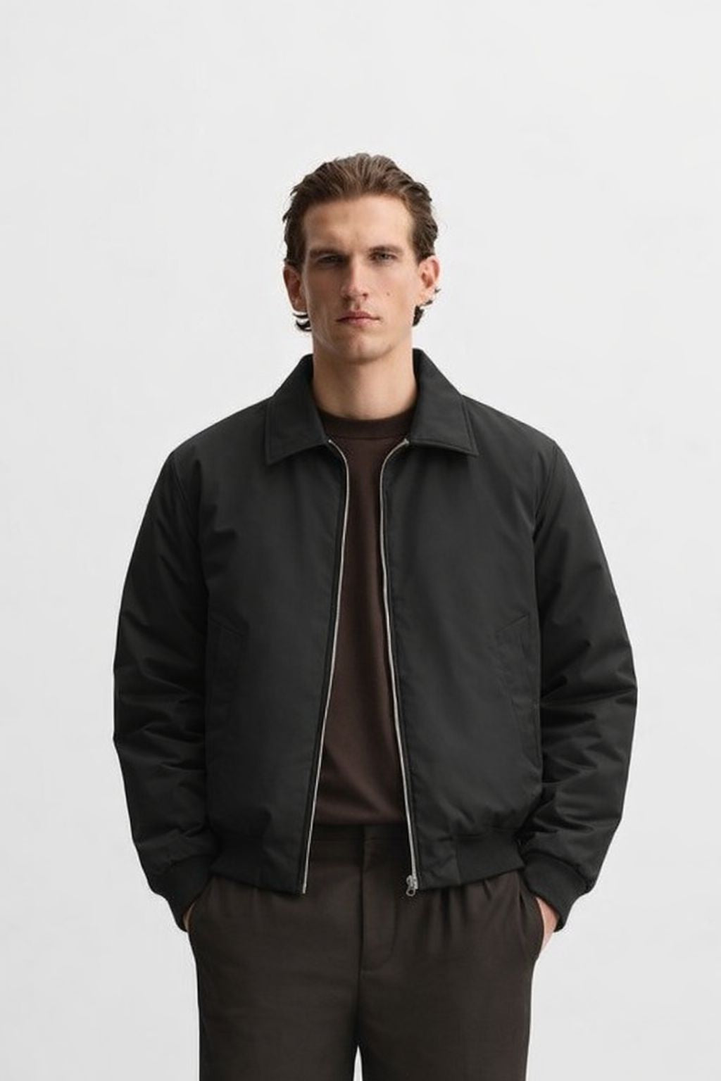 Man wearing a black bomber jacket and brown shirt against a white background