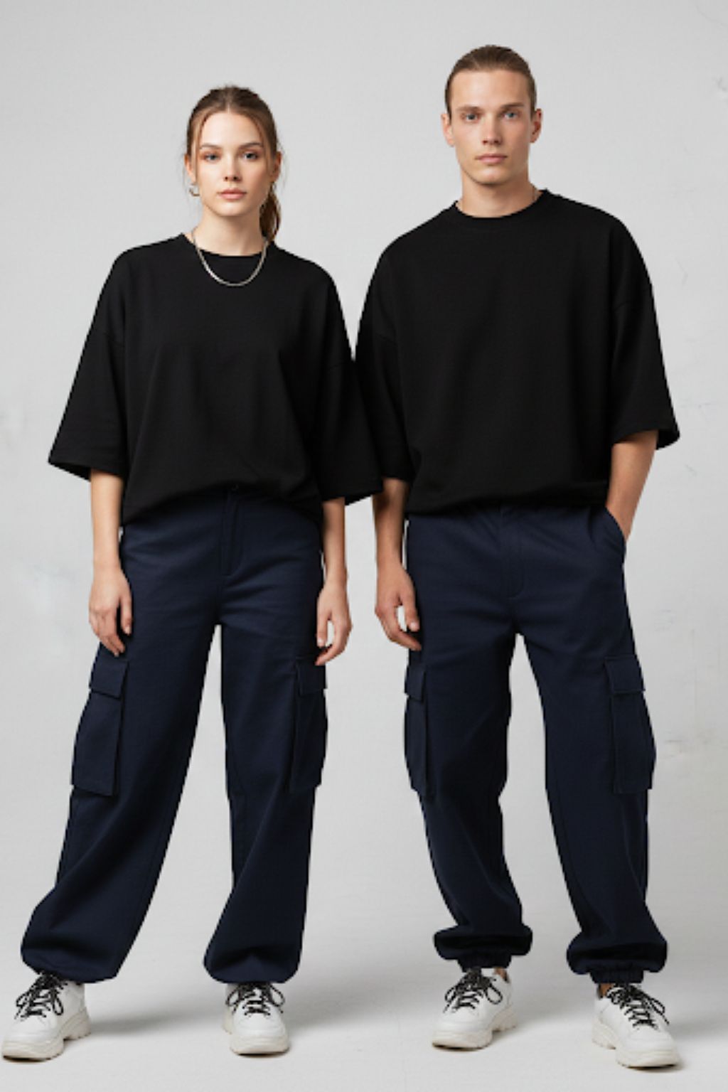 Two people wearing black tops and navy pants on a plain background