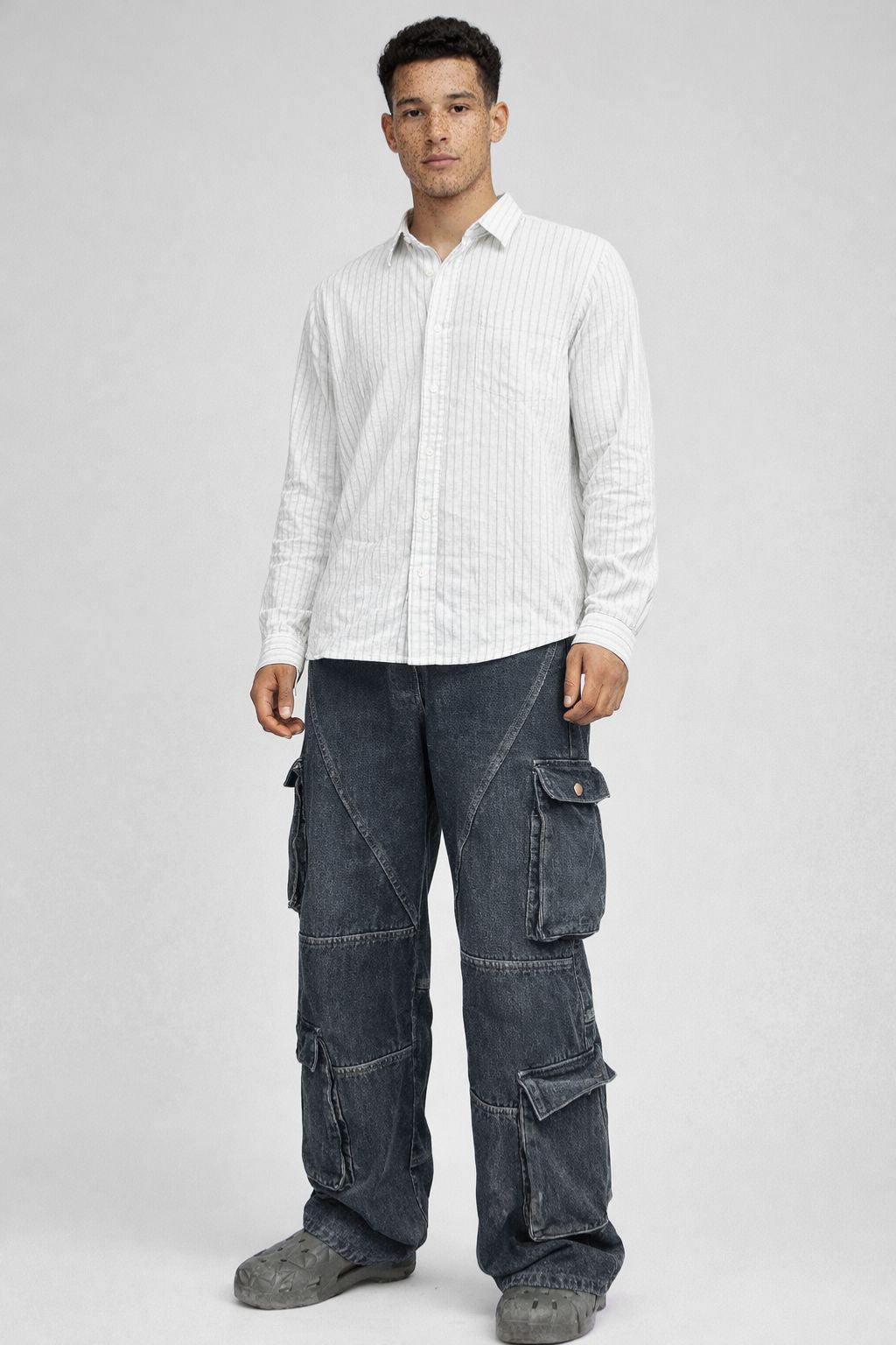 Man wearing a white striped shirt and dark cargo pants on a gray background