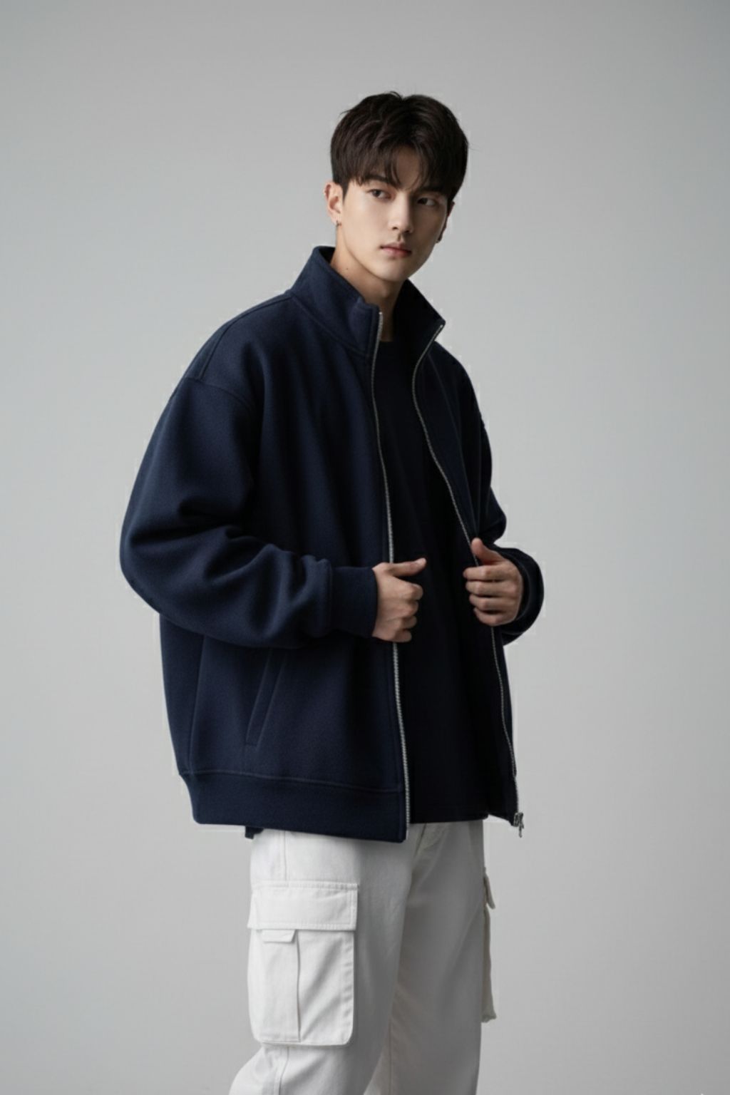 Man wearing a navy jacket and white pants against a gray background